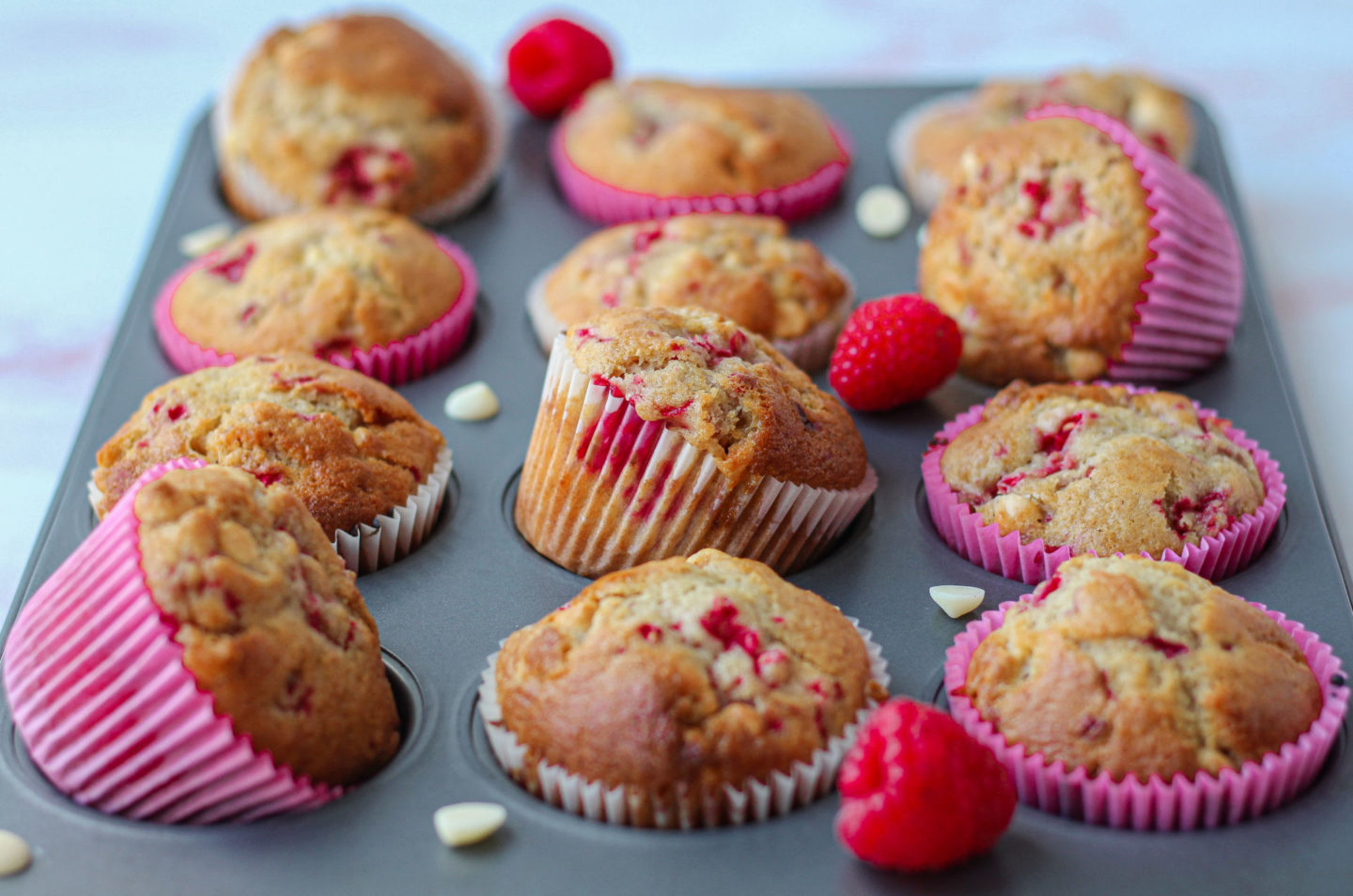 muffin tray filled with raspberry white chocolate muffins placed at different angles