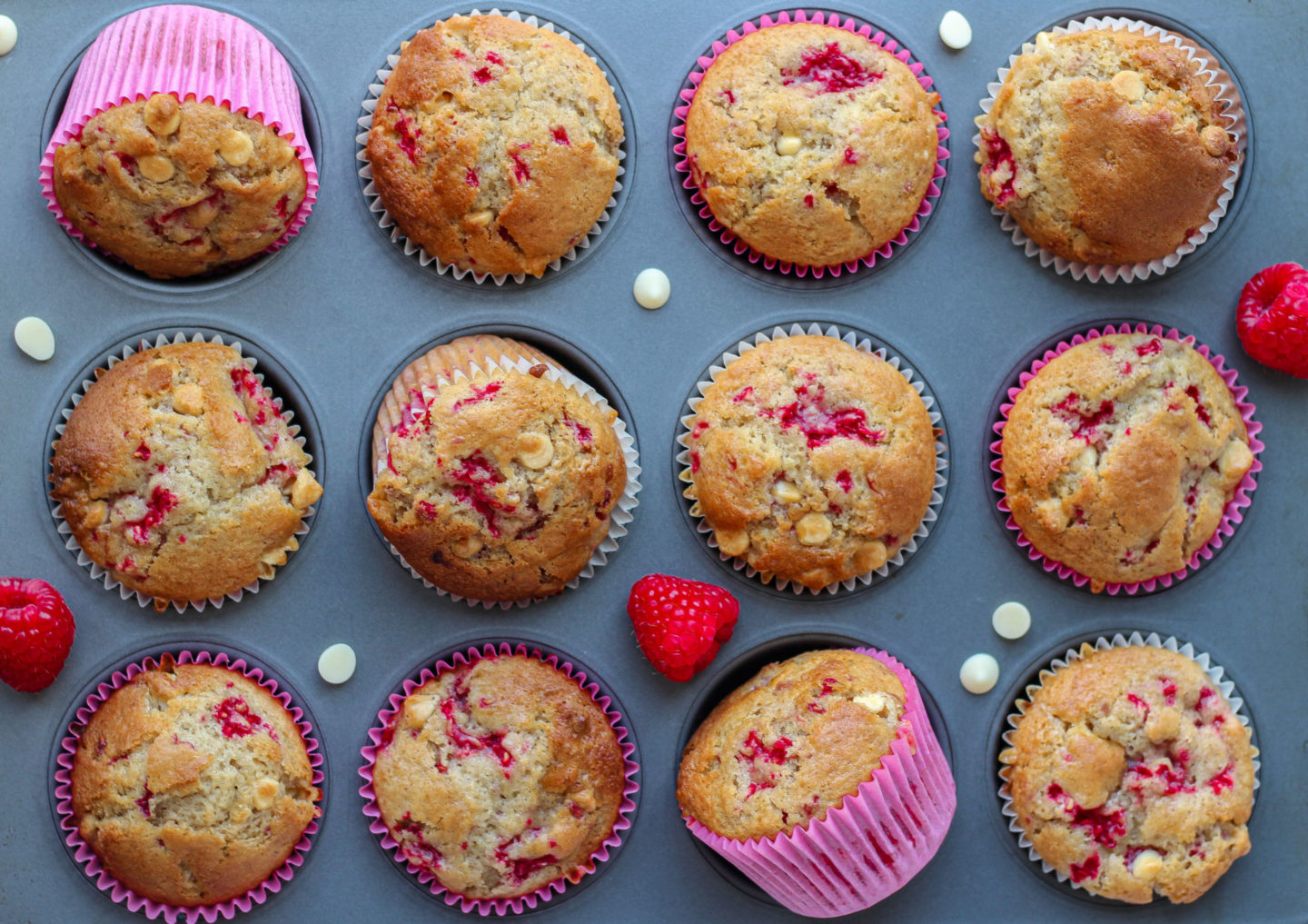 raspberry white chocolate muffins placed in a muffin tray decorated with some fresh raspberries and white chocolate chips