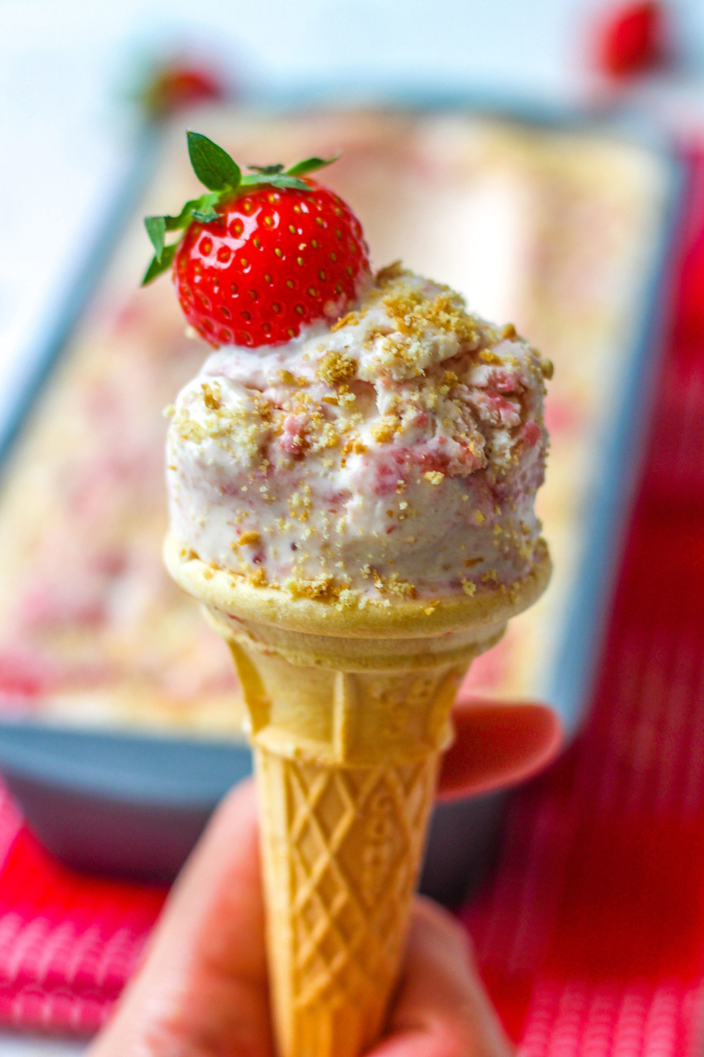 ice cream cone of strawberry cheesecake ice cream, topped with a fresh strawberry