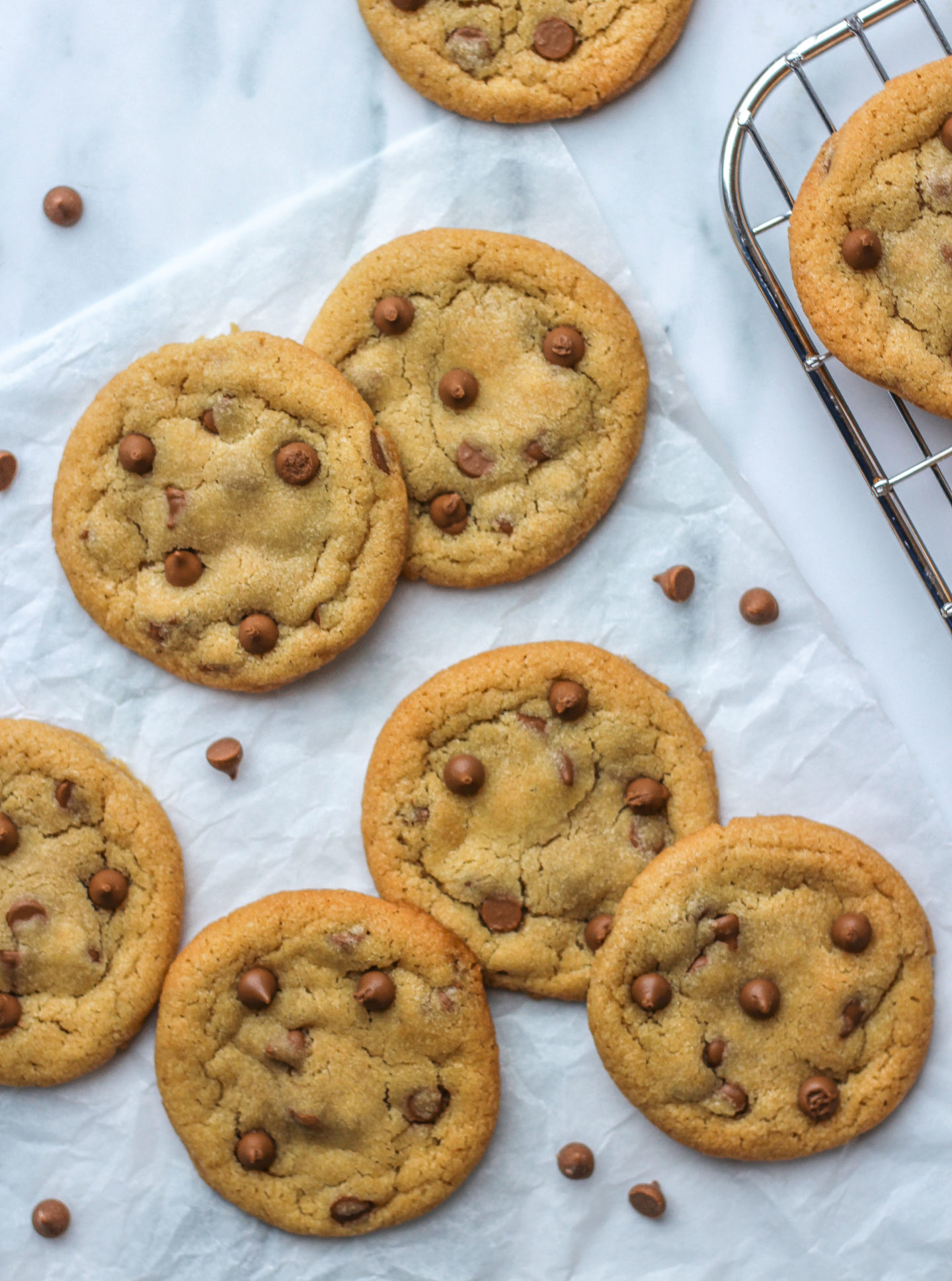 View from above of several chocolate chip cookies on parchment paper on work surface.