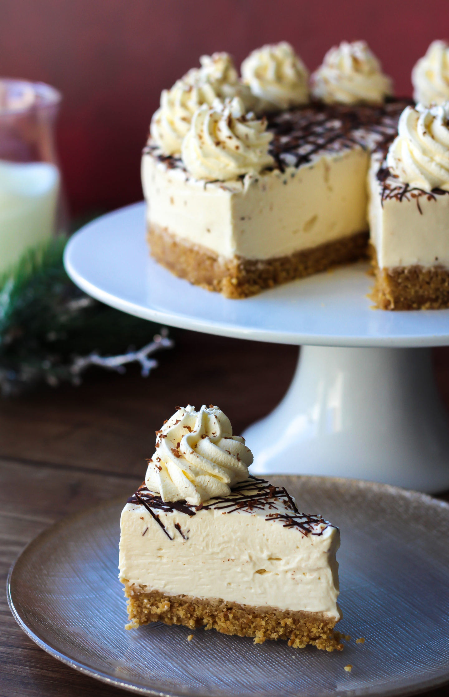 Slice of no-bake Baileys cheesecake with rest of cheesecake on a cake stand in the background