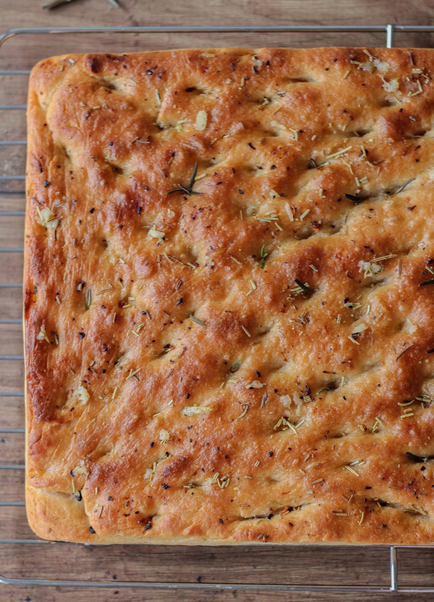 view from above of whole garlic and rosemary focaccia on wire rack