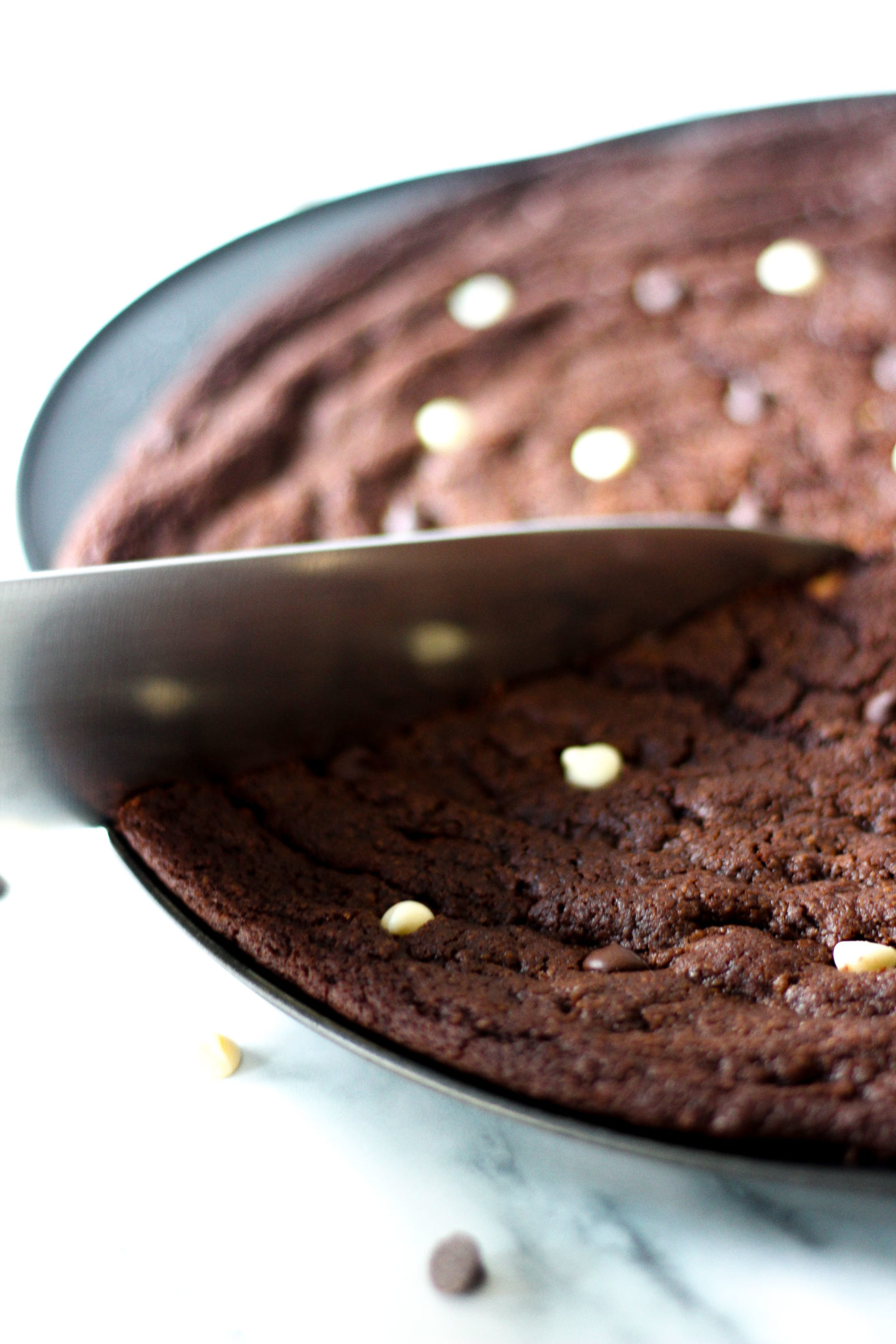 close up of knife cutting into triple chocolate chip cookie pizza in pizza pan