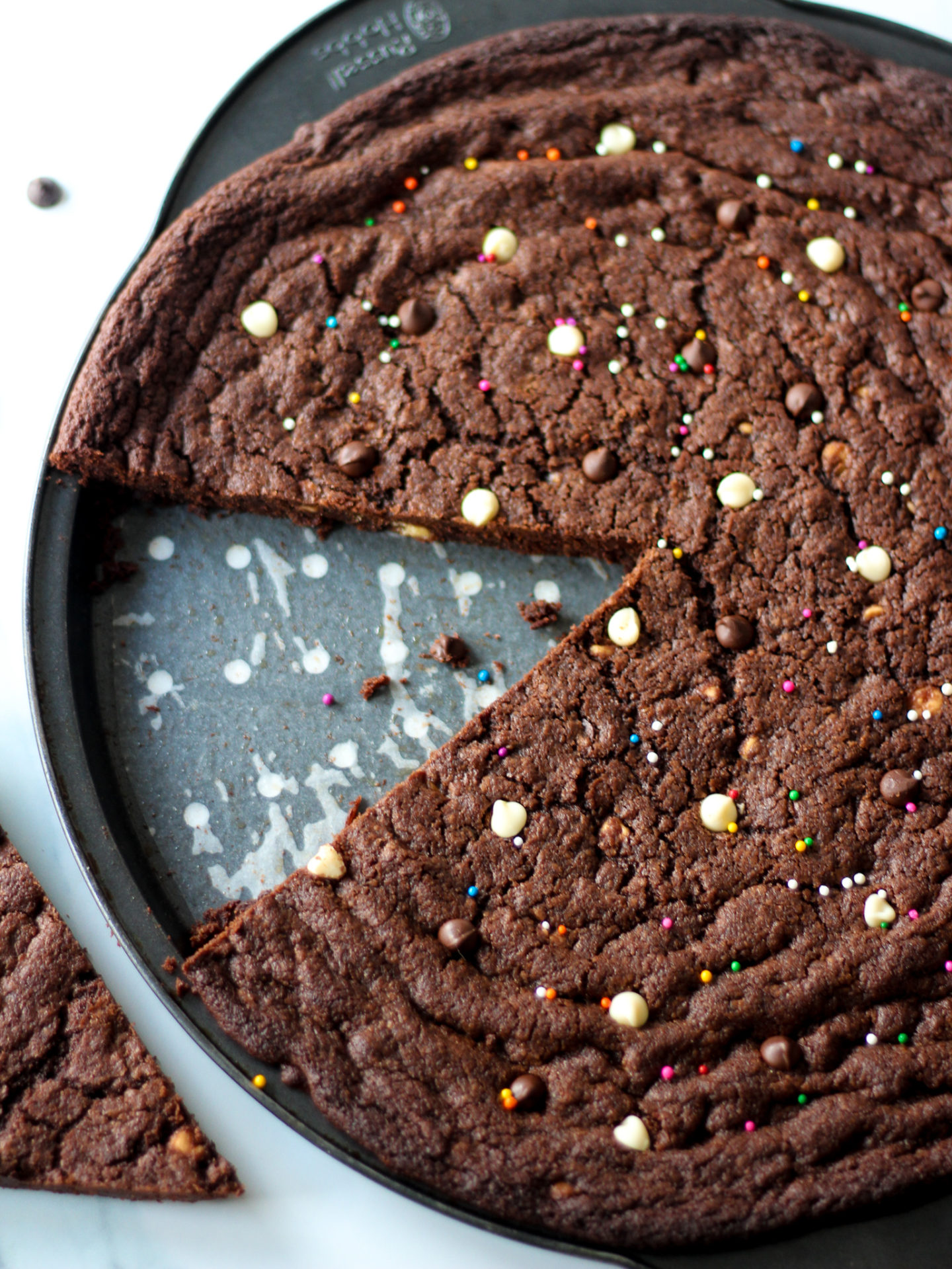 sliced triple chocolate chip cookie pizza in pan, topped with colourful sprinkles