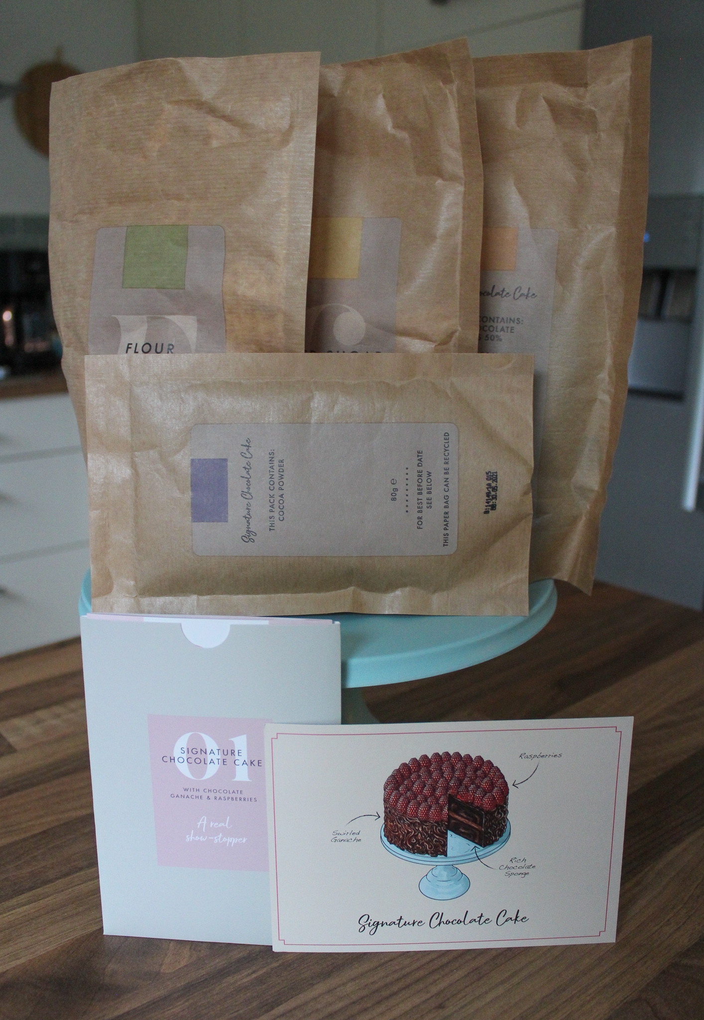 All of the pre-measured dry ingredients in unopened bags, sat on top of the blue bamboo cake stand, with recipe card at front.