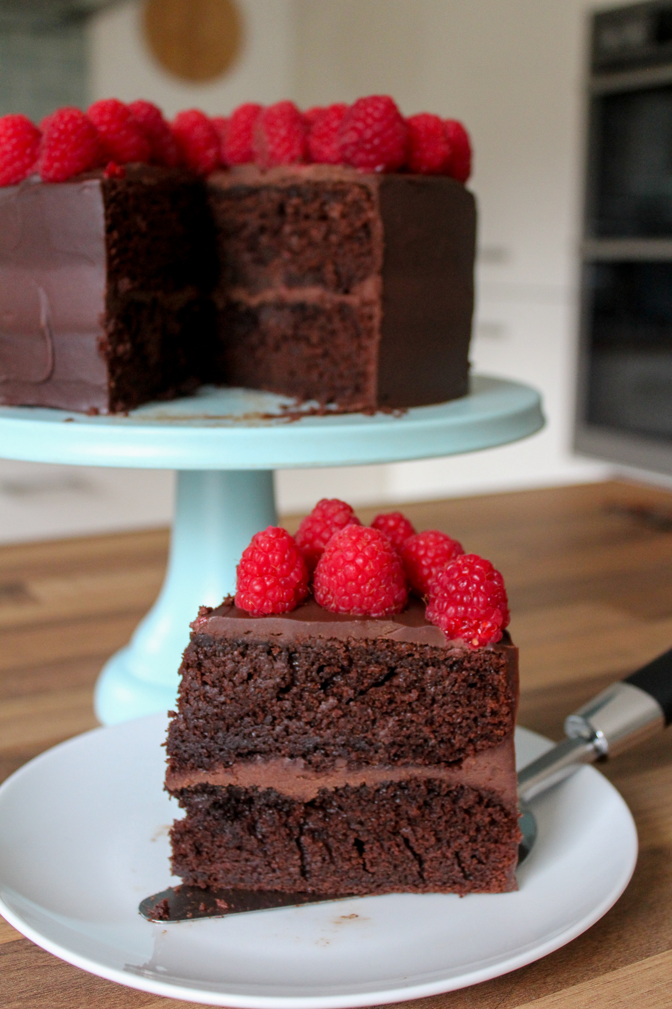 close up of slice of signature chocolate cake with cake on stand in background