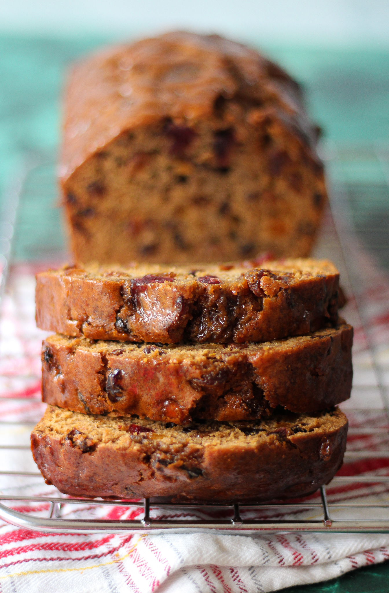 close up of three slices of bara brith on wire rack, with rest of bara brith loaf blurred in background
