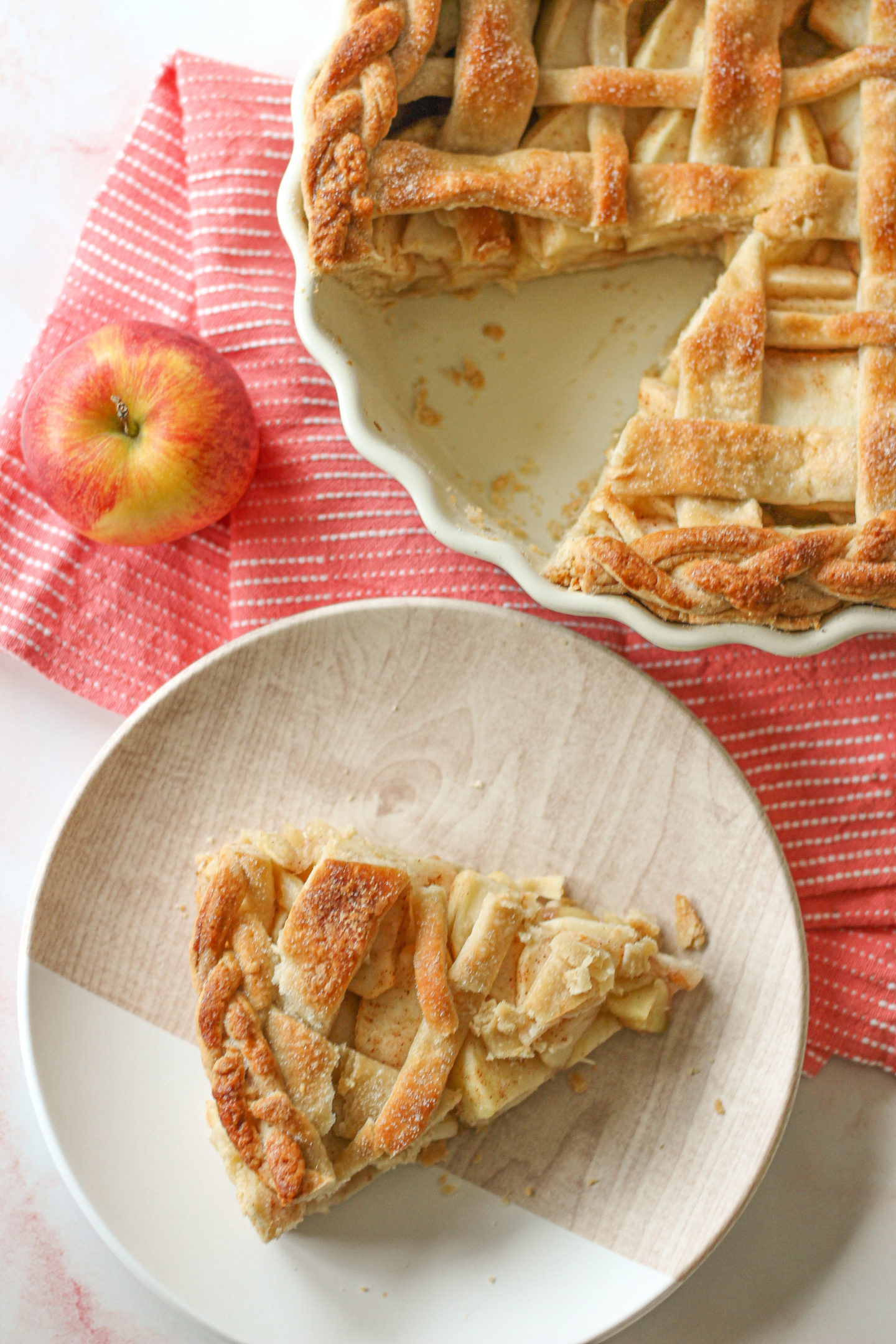 overhead view of a slice of lattice apple pie with part of the pie in the pie dish shown above it