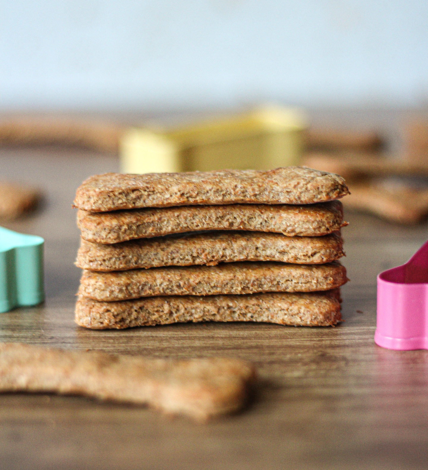 five peanut butter banana dog treats stacked on top of each other, with other treats and cookie cutters blurred in background