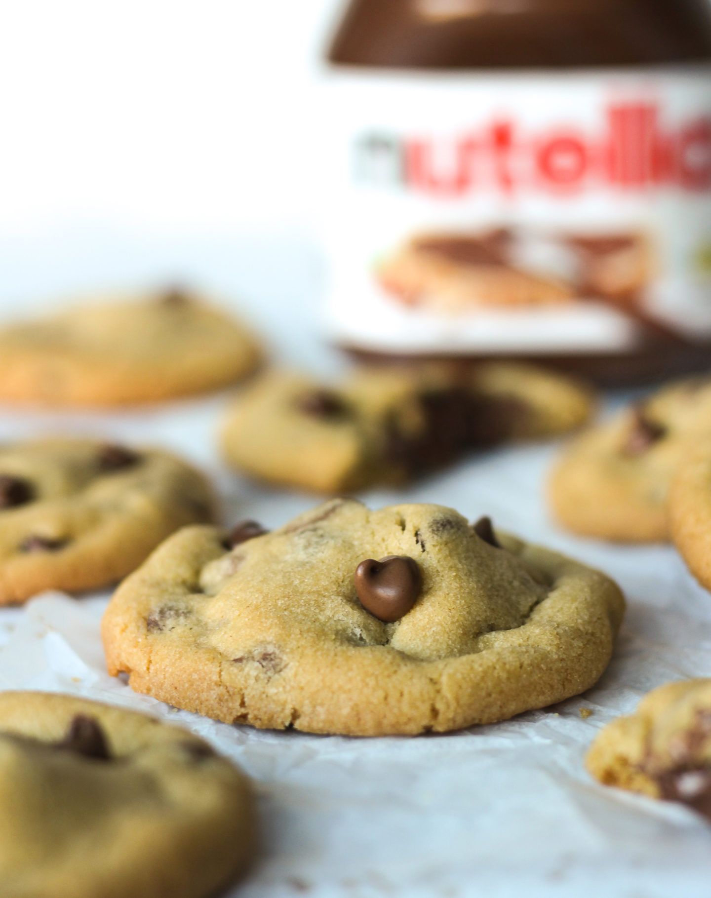 close up of  Nutella stuffed chocolate chip cookie from side showing the thick centre, with jar of Nutella in background