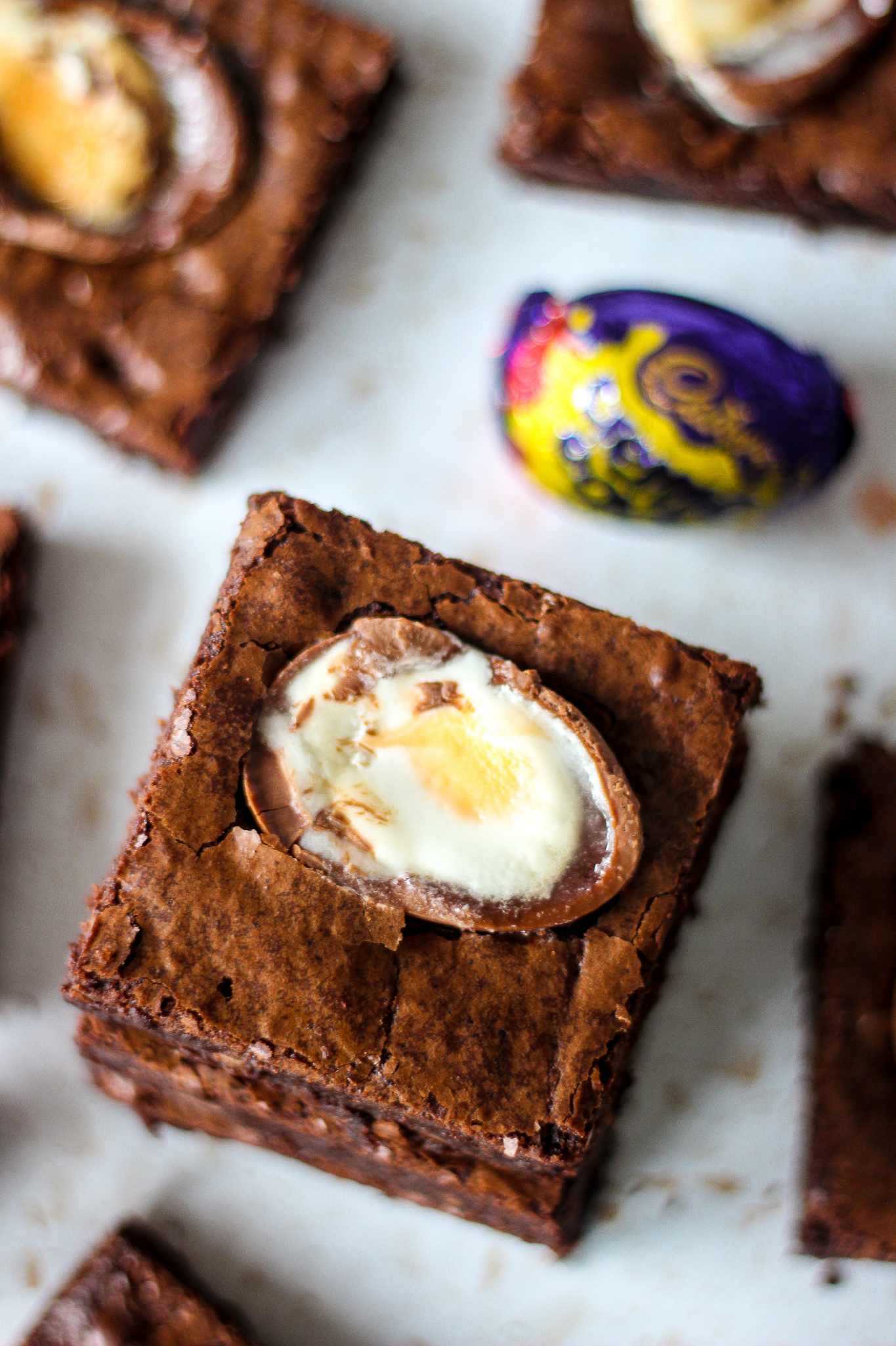 view from above of chewy creme egg brownie on top of stack of brownies. Creme Egg and other brownie slices blurred in background.