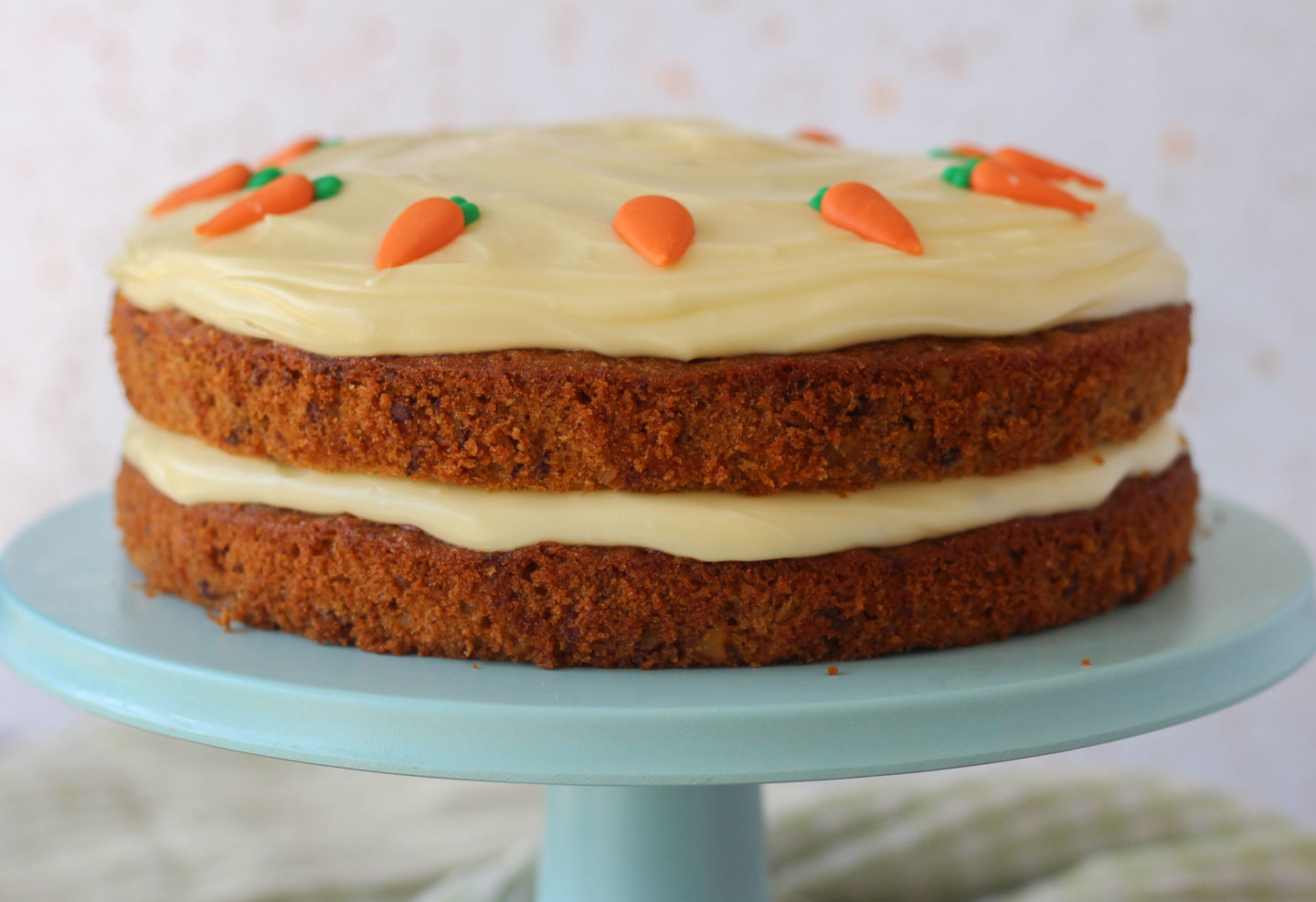 Unsliced carrot layer cake on a blue cake stand