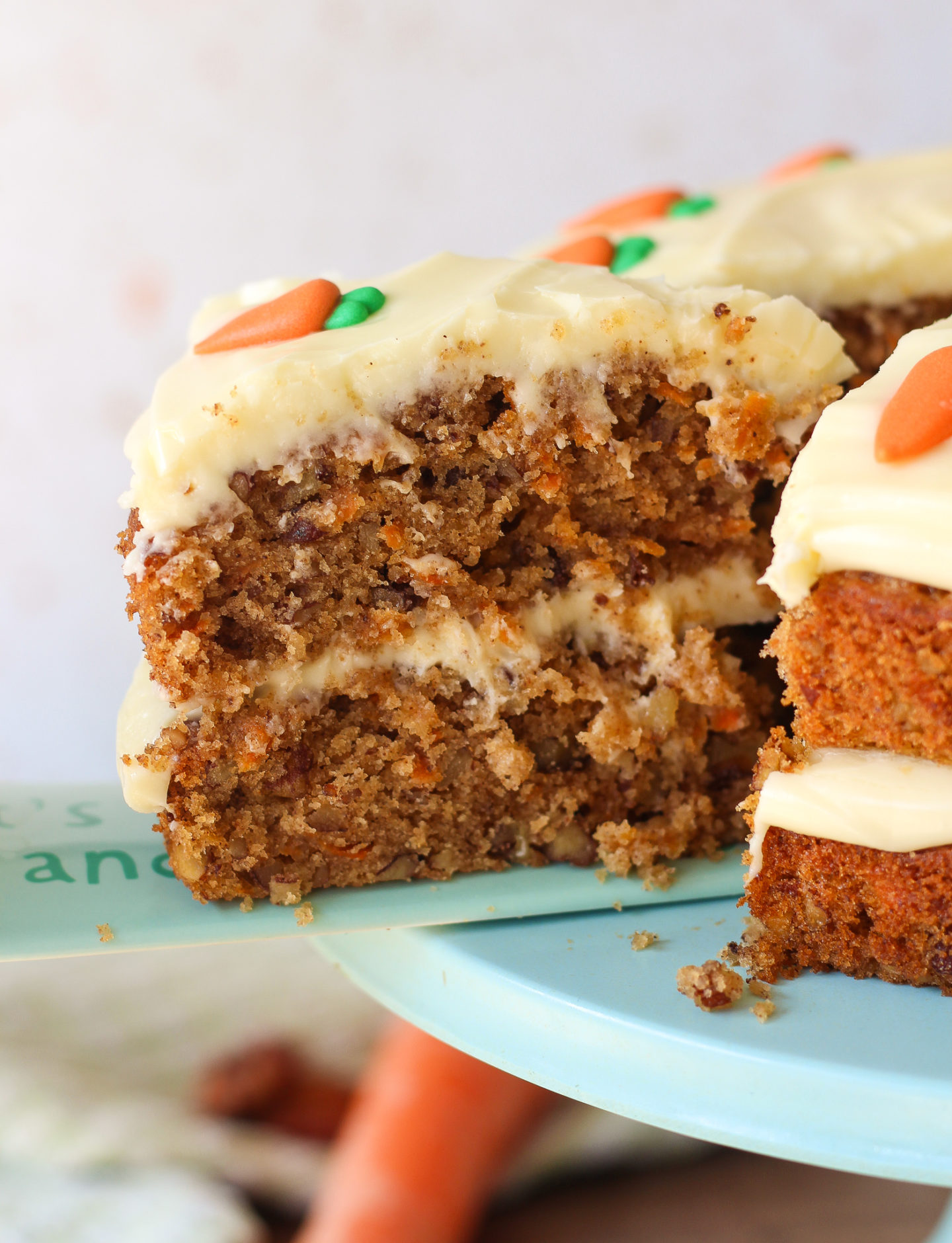 close up of a slice of carrot cake coming away from the rest of the carrot cake on a blue serving spatula
